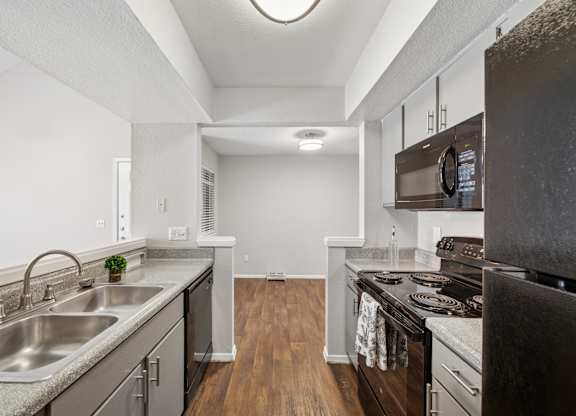 A kitchen with a stainless steel sink and black appliances.