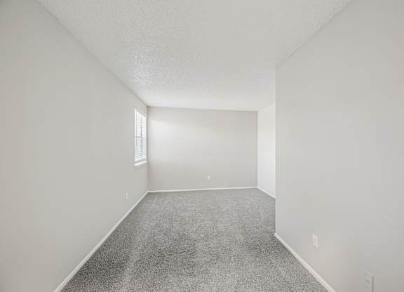 A spacious empty room with carpeted floor and white walls.