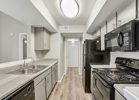 A kitchen with black appliances and a wooden floor.