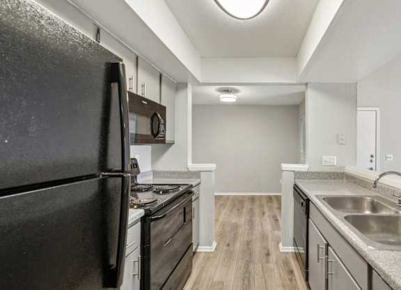 A black refrigerator is in a kitchen with wood floors and stainless steel appliances.