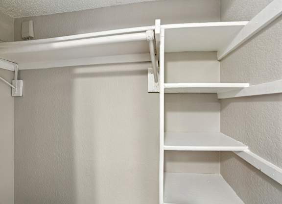 A white shelving unit with four shelves is mounted on a white wall.