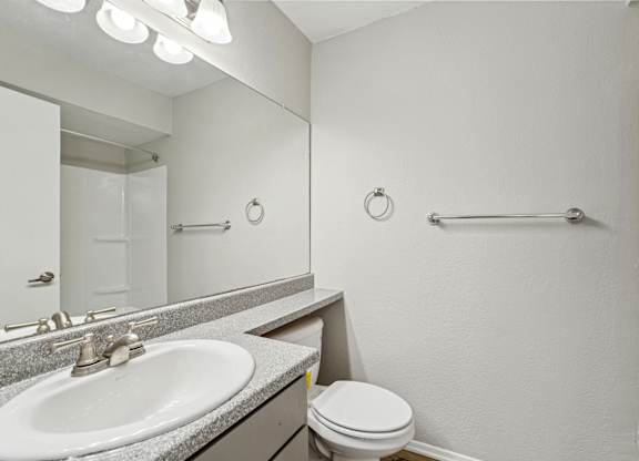A bathroom with a toilet, sink, mirror, and towel rack.