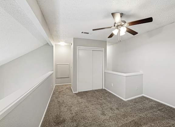 A room with a ceiling fan and carpeted floor.