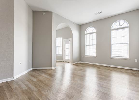 A room with wooden flooring and two windows.