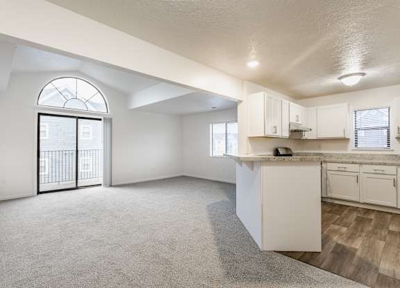 A spacious, empty room with a kitchenette and a large window with a view of a balcony at Huntington Cove Apartments, Merrillville, IN, 46410