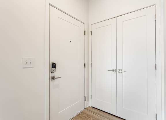 A white door with a keypad lock is open to a hallway with three white doors at Upper Vue Flats, Dublin