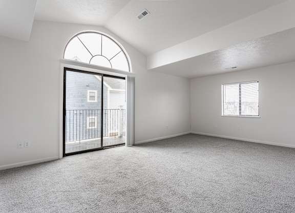 A spacious room with a large arched window and a sliding glass door leading to a balcony at Huntington Cove Apartments, Merrillville, IN, 46410