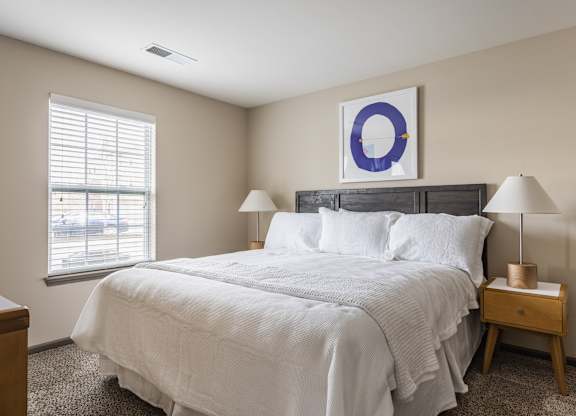 A bedroom with a large bed and a window with blinds.
