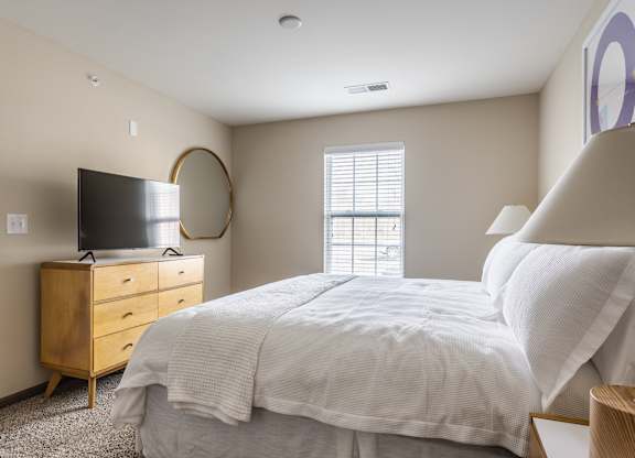 A bedroom with a large bed, a television, and a window.