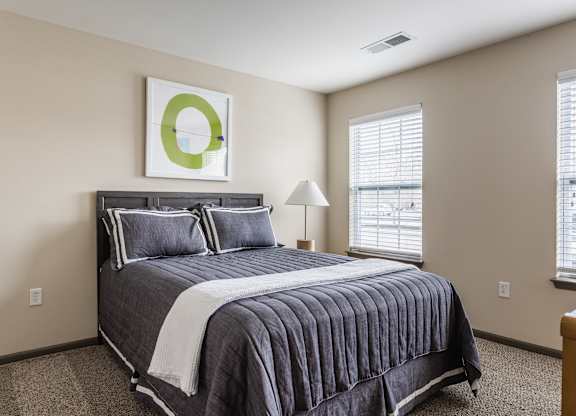 A bedroom with a bed, pillows, a lamp, and a picture on the wall.