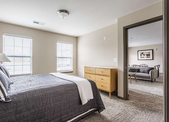 A bedroom with a large bed, a dresser, and a window with blinds.