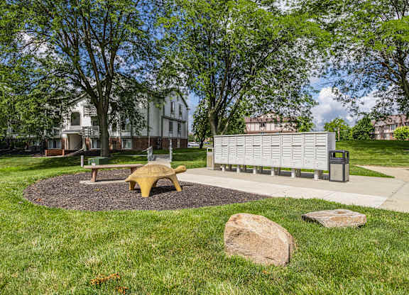 A park with a bench, a tree, and a rock.