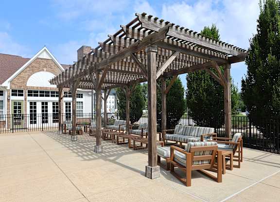 A wooden pergola with striped cushioned seating is in front of a building.