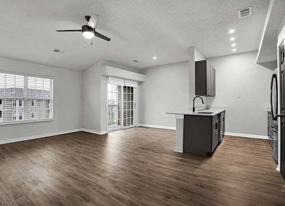 an empty living room with a kitchen and a ceiling fan at Latitudes Apartments, Indianapolis, IN