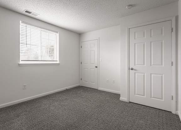 an empty living room with a white door and a window at Latitudes Apartments, Indianapolis, IN