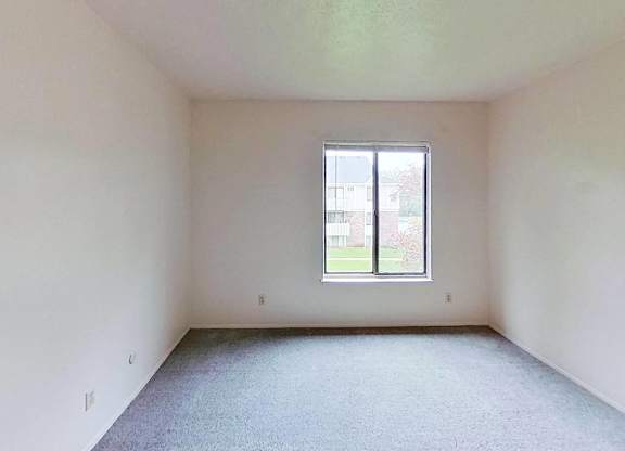 A bedroom with a window and carpeted floor at Briarwood Apartments in Benton Harbor, MI