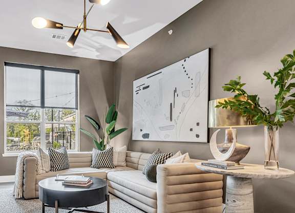 A modern living room with a large window, a sofa, a coffee table, and a potted plant.