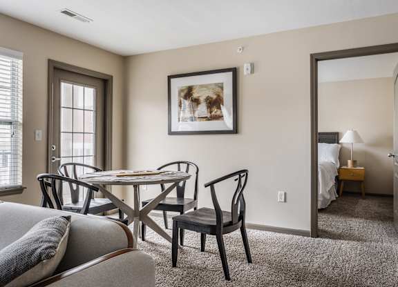 A living room with a grey couch, a round table with four chairs, and a painting on the wall.