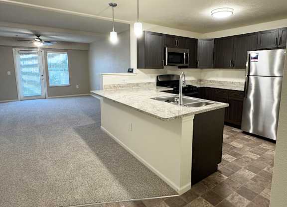 A kitchen with a breakfast bar and a living room at Andover Pointe Apartment Homes in LaVista, NE