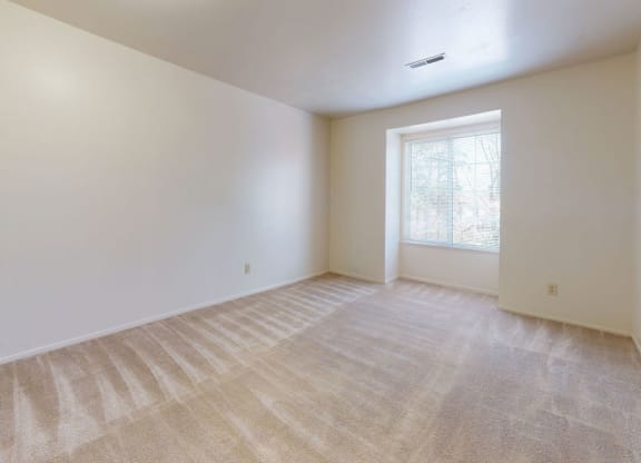 an empty bedroom with a large window and plush carpet at Apple Ridge Apartments, Michigan, 49534