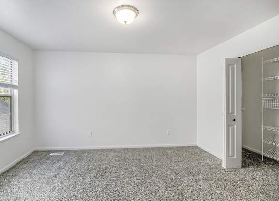 A room with a carpeted floor, a window with blinds, a door, and a ceiling light fixture at Autumn Lakes Apartments and Townhomes, Mishawaka, 46544