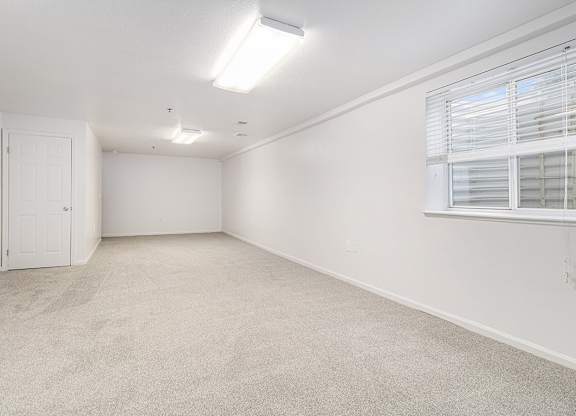 A finished basement recreation room with a carpeted floor and a window with blinds at Autumn Lakes Apartments and Townhomes, Mishawaka, 46544