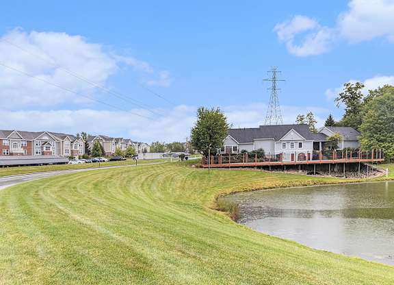A grassy area with a pond and buildings in the background at Autumn Lakes Apartments and Townhomes, Mishawaka, IN