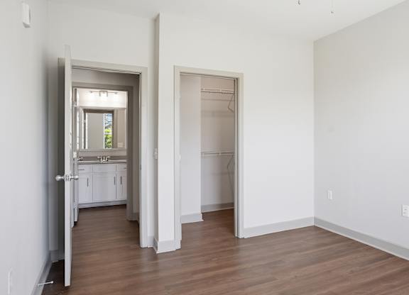 A room with white walls and wooden floors, with a doorway leading to another room.