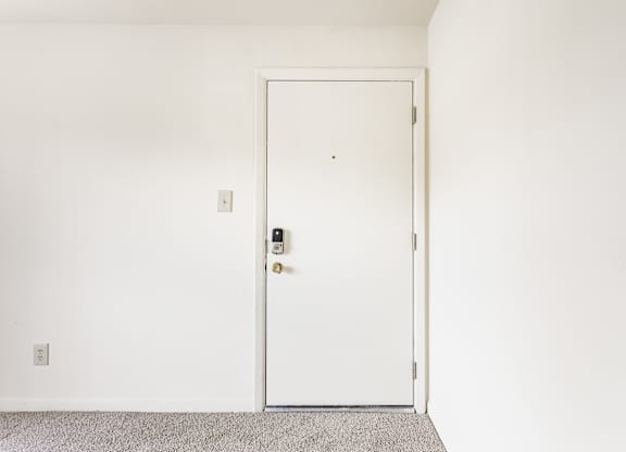 A white door with a handle and a keypad is in a room with a grey carpet