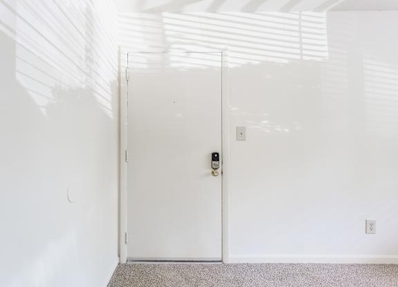 A white door with a black handle and lock in a white room