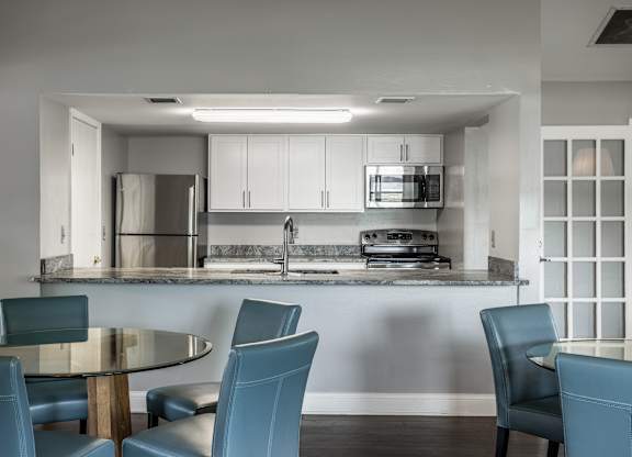 A modern kitchen with a glass table and blue chairs.