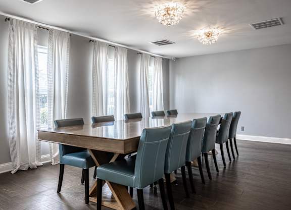 A long wooden table with blue chairs is in the middle of a room with a window.
