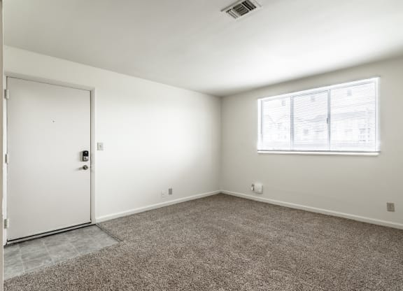 an empty room with carpet and a window and a door at Bay Pointe Apartments in Lafayette, IN