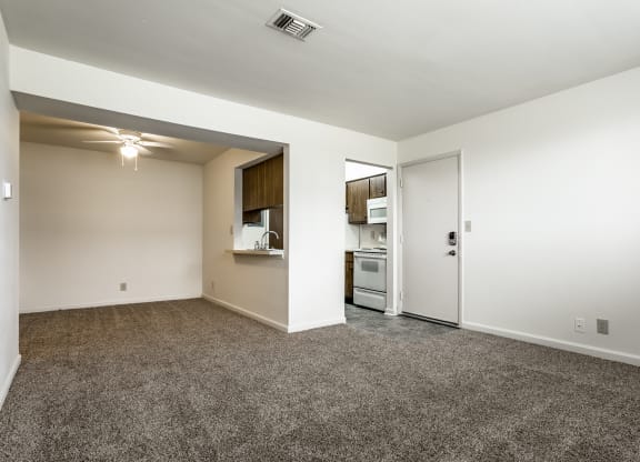 an empty living room with carpet and a door to a kitchen at Bay Pointe Apartments in Lafayette, Indiana