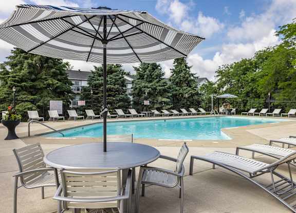 A pool area with a table and chairs and an umbrella.