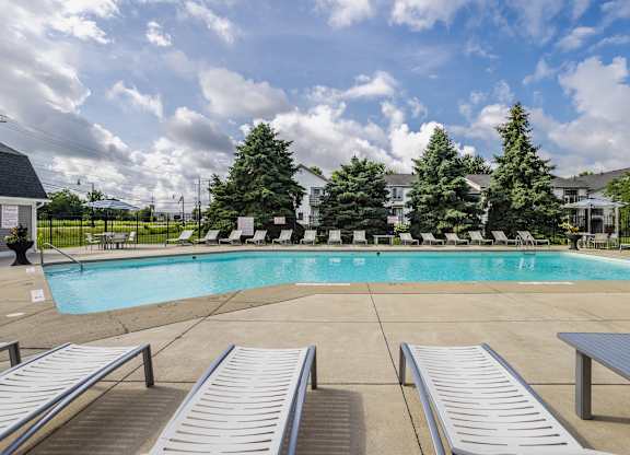 A pool surrounded by trees and chairs.