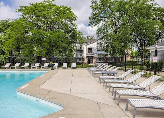 A pool surrounded by trees and lounge chairs.