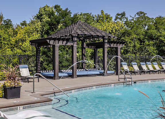 A pool with a gazebo and lounge chairs.