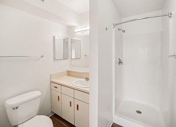 A white bathroom with a shower, toilet, sink and mirror at Black Sand Apartments Homes, Lincoln, NE