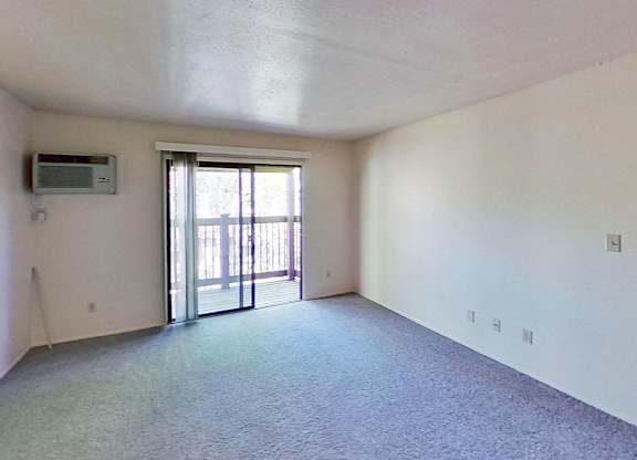 A living room with a carpeted floor and a sliding glass door leading to a balcony at Briarwood Apartments in Benton Harbor, MI