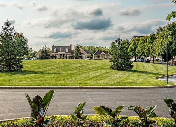 A large building is surrounded by a green lawn and trees