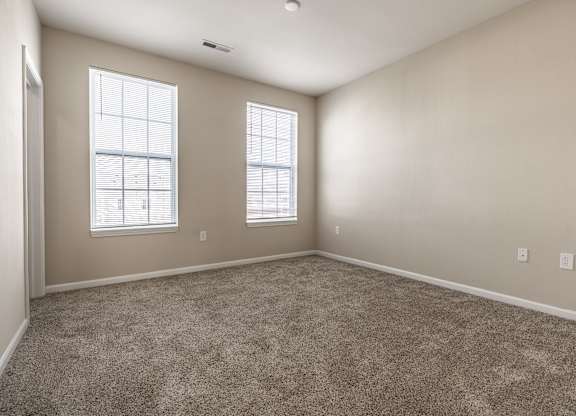 A spacious room with carpeted floor and two windows
