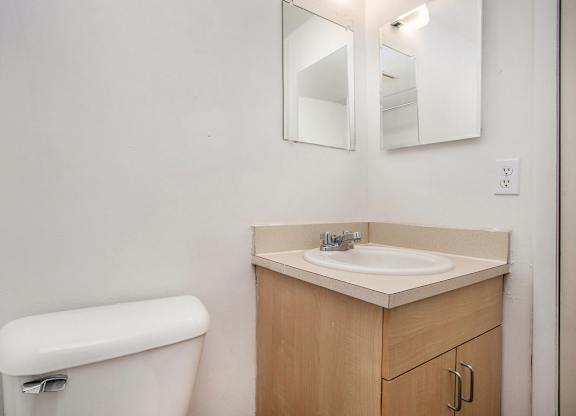 A toilet sits next to a sink with a mirror above it in a bathroom at Brookside Apartments, Springfield