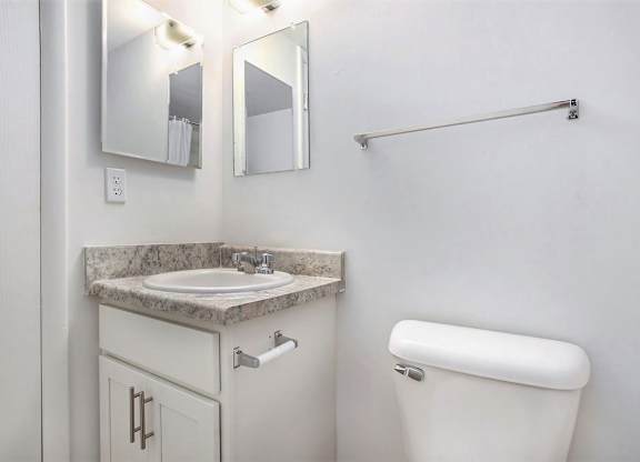 A bathroom with a white cabinet, sink, mirror, toilet and towel bar at Brookside Apartments, Springfield
