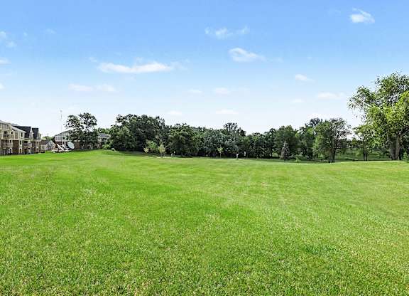 A large grassy field with trees and houses in the background.