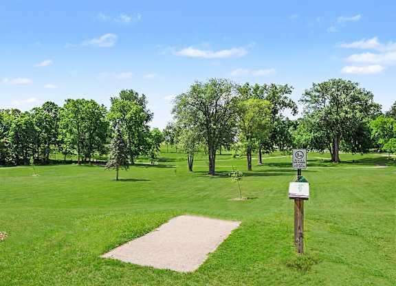 A sign in a grassy field with trees in the background.