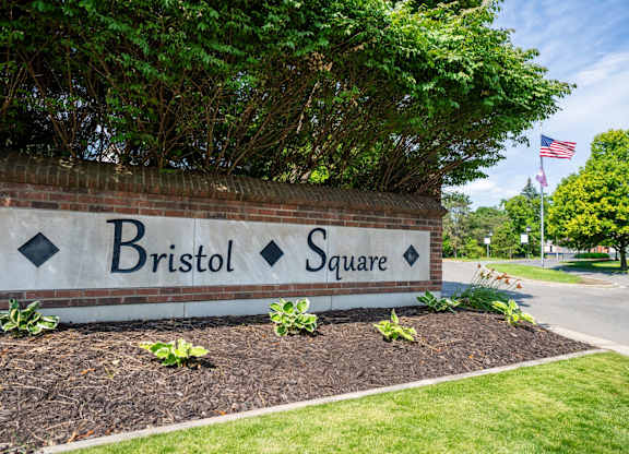 A sign that says Bristol Square is in front of a brick wall.