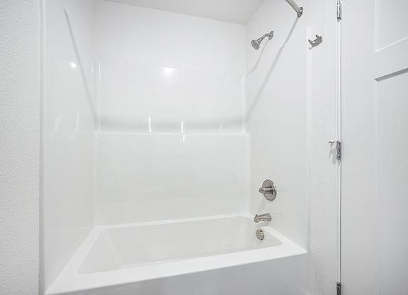 A white bathroom with a tub and shower at Byron Lakes Apartments, Byron Center, MI