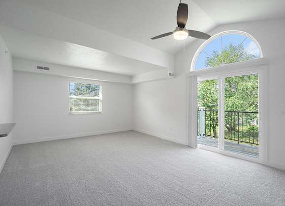 An end living room with a cathedral ceiling, ceiling fan and sliding glass doors leading to a balcony at Byron Lakes Apartments, Byron Center, Michigan