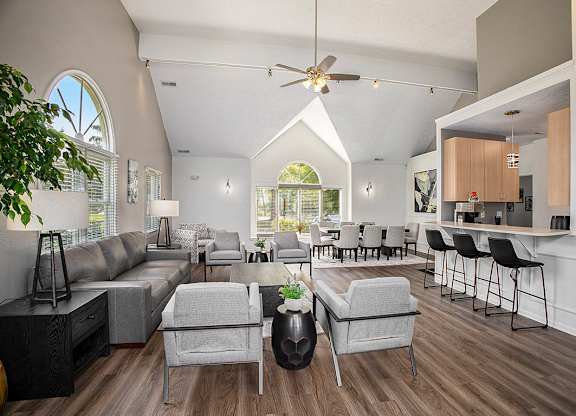 A community room with a grey sofa, armchairs and a kitchen with breakfast bar at Canal 2 Apartments in Lansing, MI
